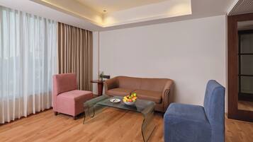 A modern living room with a brown leather sofa, a blue armchair, and a glass coffee table with fruit.
