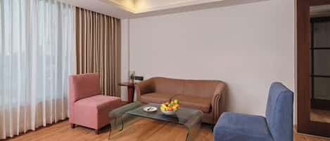 A modern living room with a brown leather sofa, a blue armchair, and a glass coffee table with fruit.