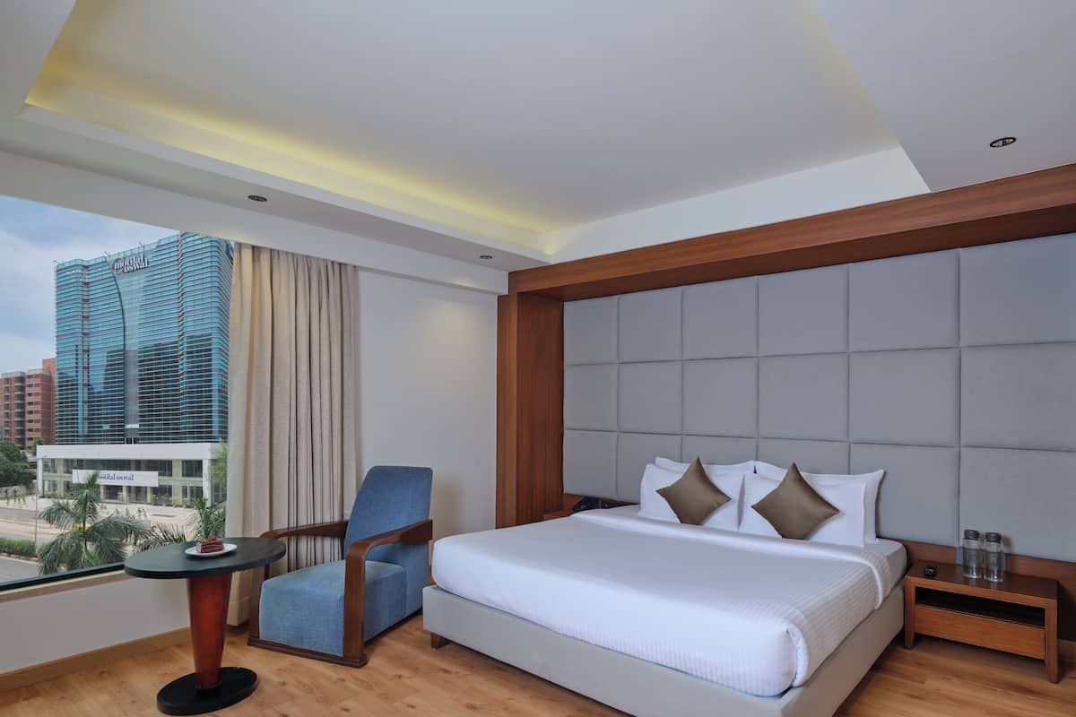 A hotel room with a large bed, a chair, a small table with a plate of food, and a view of a cityscape.