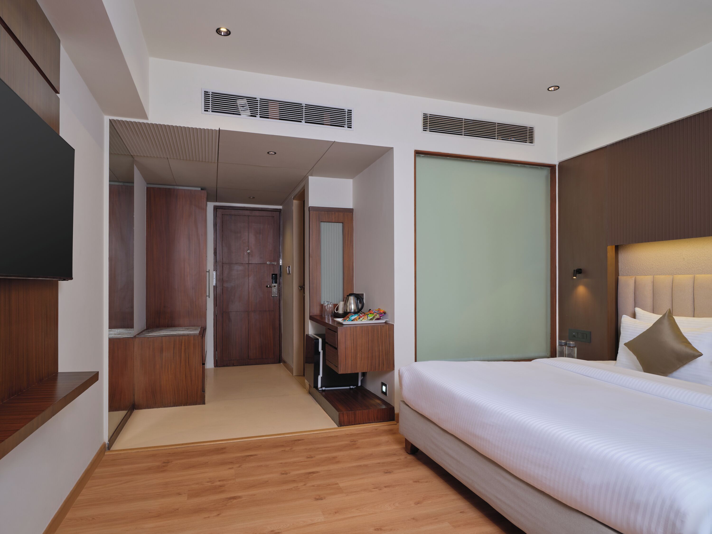 A hotel room with a bed, a desk, a mirror, a wardrobe, and a television.