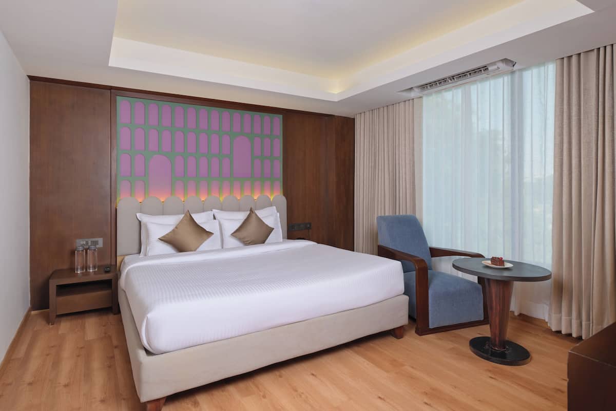 A hotel room with a bed, a chair, a small table, and a large window with curtains.