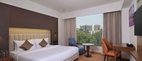 A modern hotel room with a large bed, a desk, a chair, and a small table.