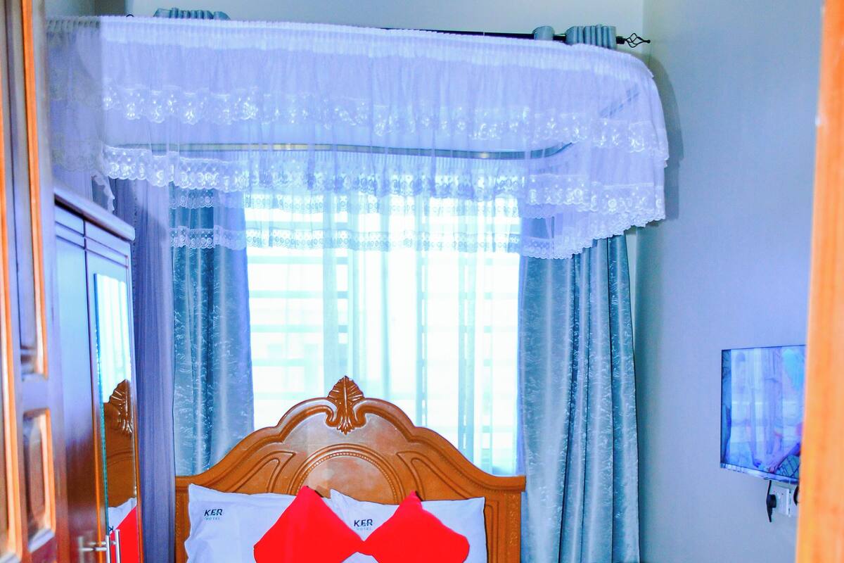 Ein Hotelzimmer mit Bett, Sessel, Fernseher und einem Fenster mit Vorhängen.