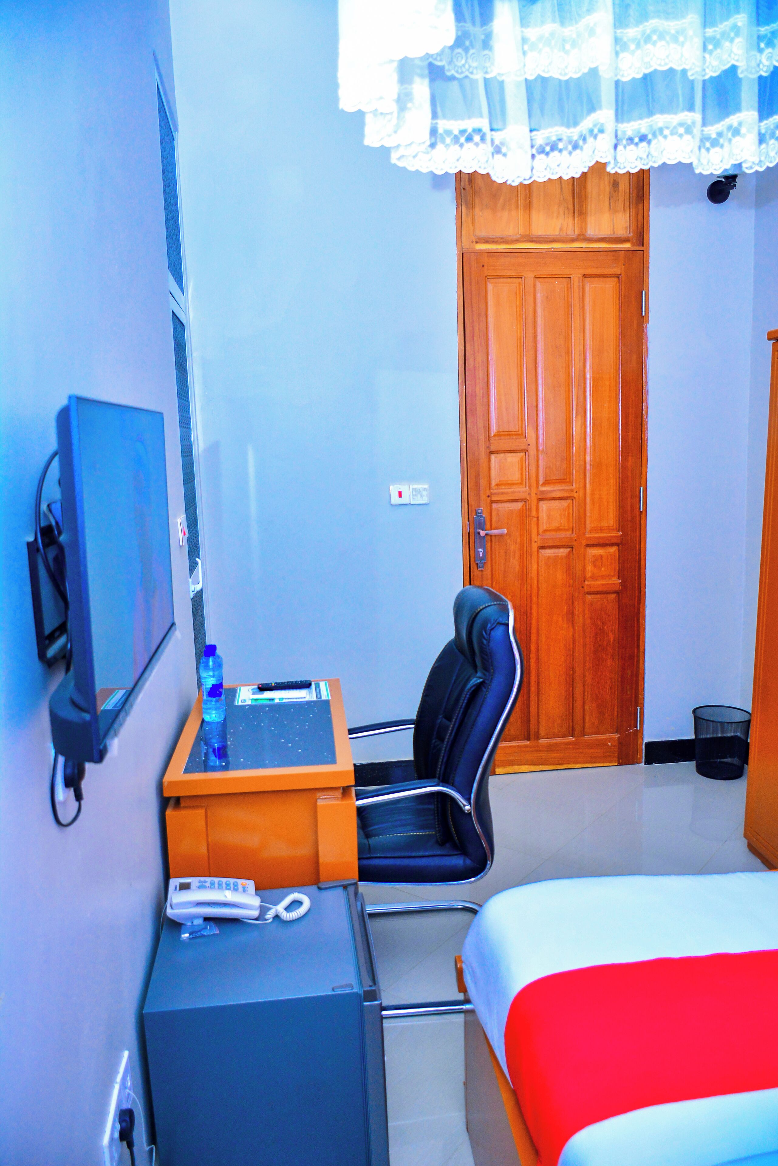 A hotel room with a bed, a desk with a chair, a telephone, a water bottle, and a television.