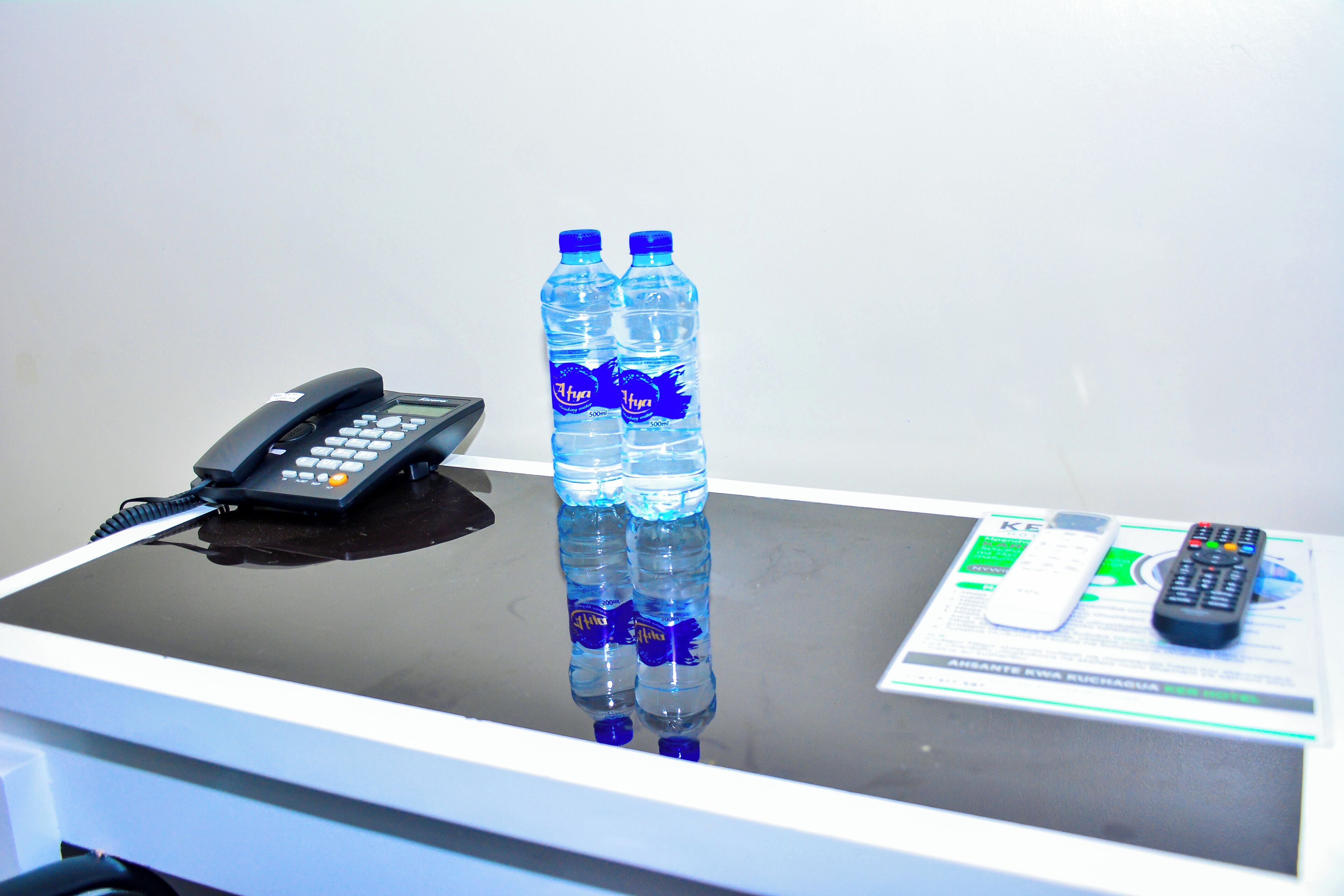 A desk with a telephone, two water bottles, and a remote control.