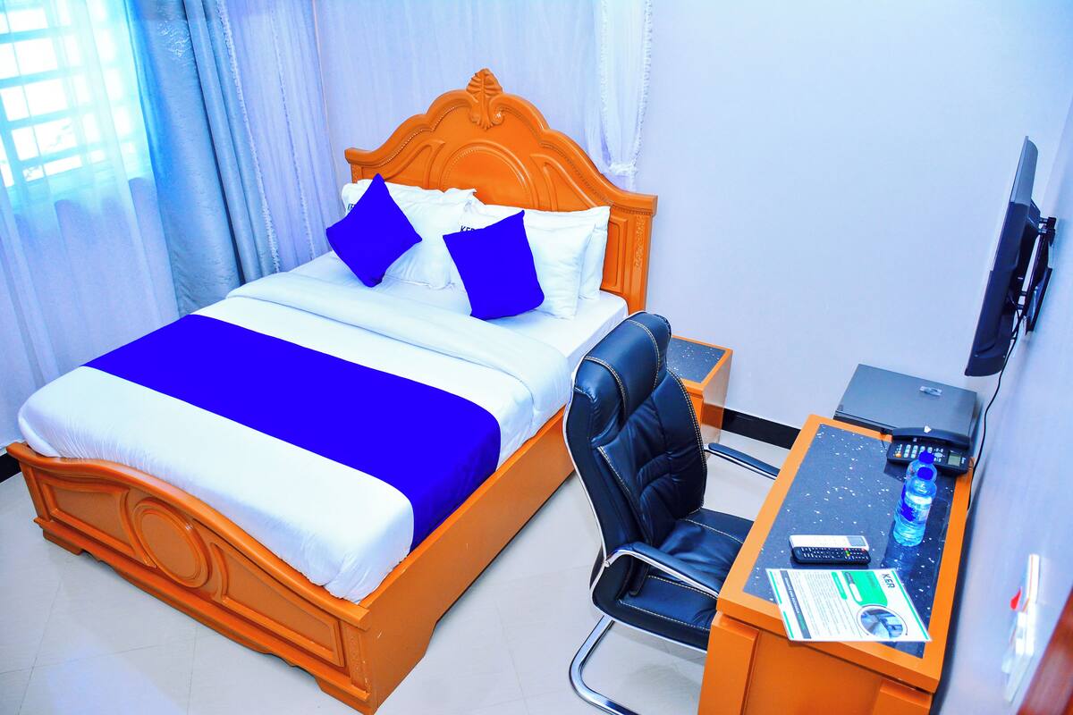 Ein Hotelzimmer mit Bett, Schreibtisch, Stuhl, Laptop und Fernseher.