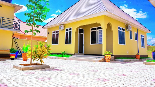A yellow building with a tiled patio, air conditioning units, and potted plants. - KER HOTEL DODOMA (Dodoma)