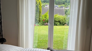 A bedroom with a bed, a view through a sliding glass door to a garden, and a window with curtains.