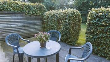 A round table with a potted plant, two chairs, and a wooden fence in a garden setting.