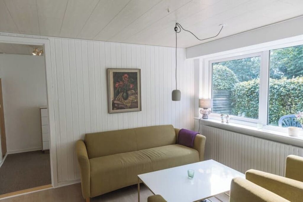 Une pièce avec un canapé beige, une table blanche et une fenêtre donnant sur un paysage verdoyant.