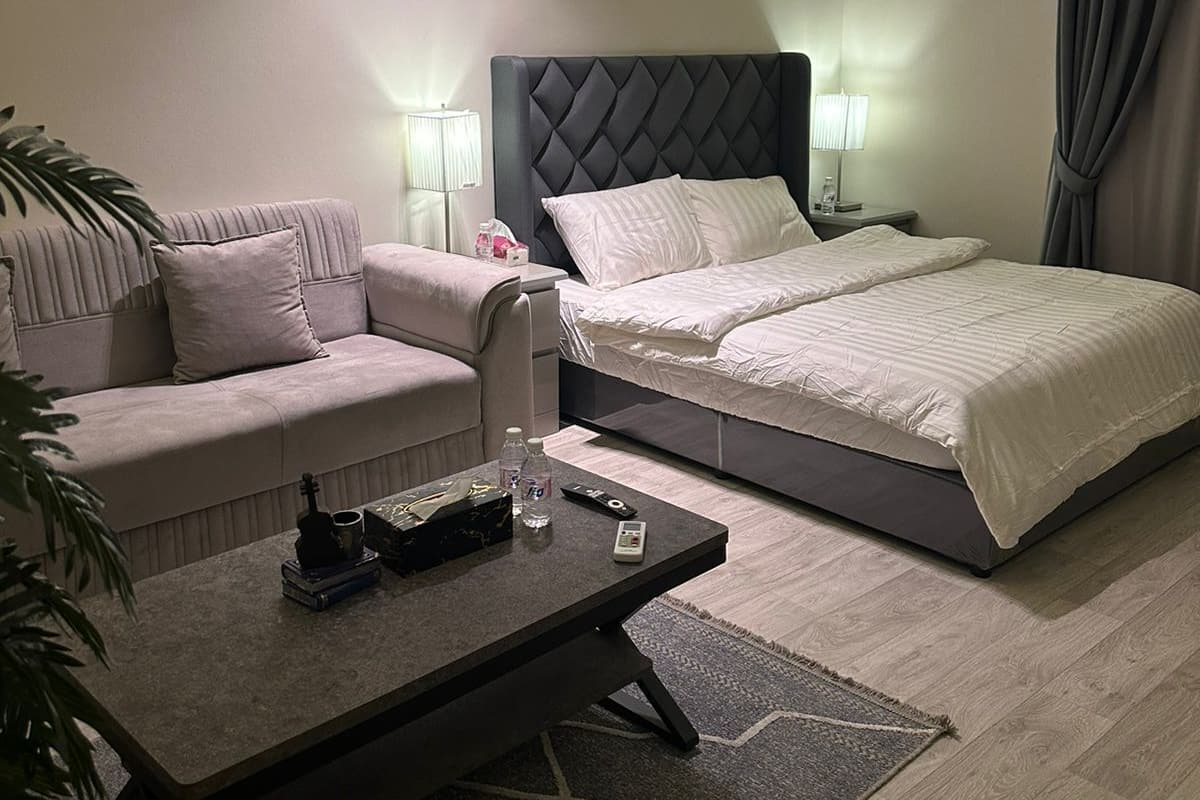 A modern hotel room with a large bed, a sofa, a coffee table, and a desk.