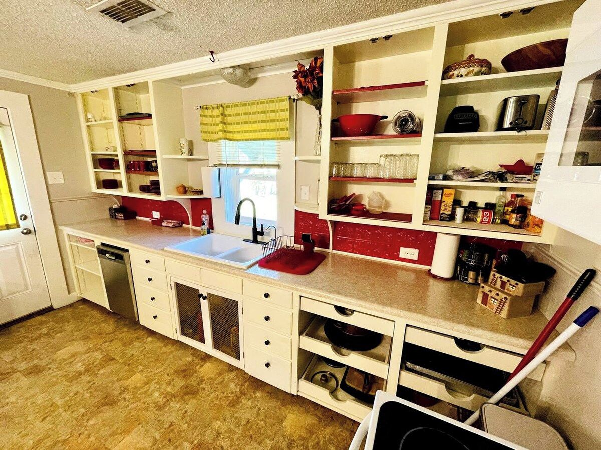 A compact kitchen with white cabinetry, a red countertop, and a built-in dishwasher.