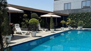 Une piscine entourée de chaises longues et de parasols, agrémentée de plantes en pot et bordée d’un bâtiment moderne.