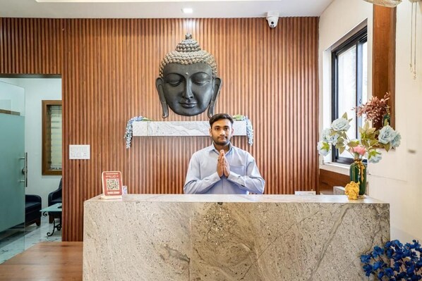 En receptionsdisk med en Buddha-staty ovanför, en vas med blommor och en QR-kod på väggen.