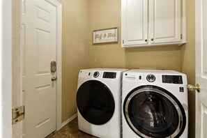 A laundry room with two front-loading washing machines, a white door, and a framed sign on the wall.