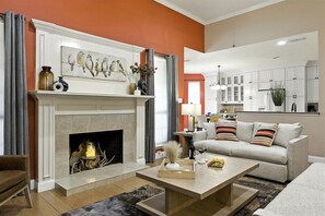 Una sala de estar con chimenea, un sofá, una mesa de centro y una zona de cocina al fondo.