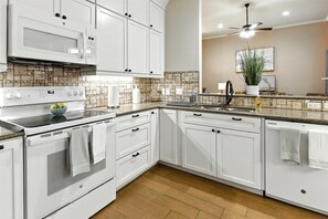 Cocina moderna con armarios blancos, microondas, estufa y lavavajillas.