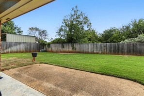 A backyard with a wooden fence, a lawn, and a gravel area.