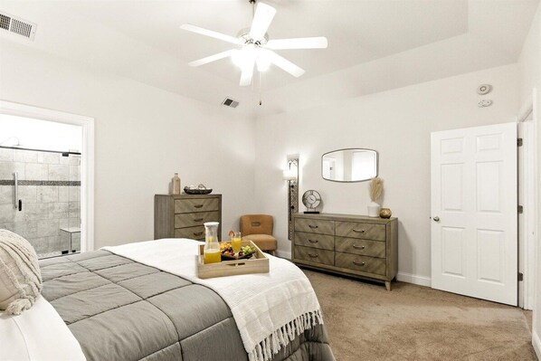 A bedroom with a bed, a dresser, a mirror, a door, and a ceiling fan.
