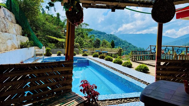 A pool area with a view of mountains, surrounded by greenery and a wooden deck. - Ventara Clouds Resort (Darjeeling)