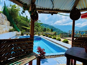 A pool area with a view of mountains, surrounded by greenery and a wooden deck. - Ventara Clouds Resort (Darjeeling)