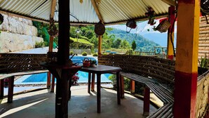 A covered outdoor area with a pool, wooden benches, and a view of a mountainous landscape. - Ventara Clouds Resort (Darjeeling)