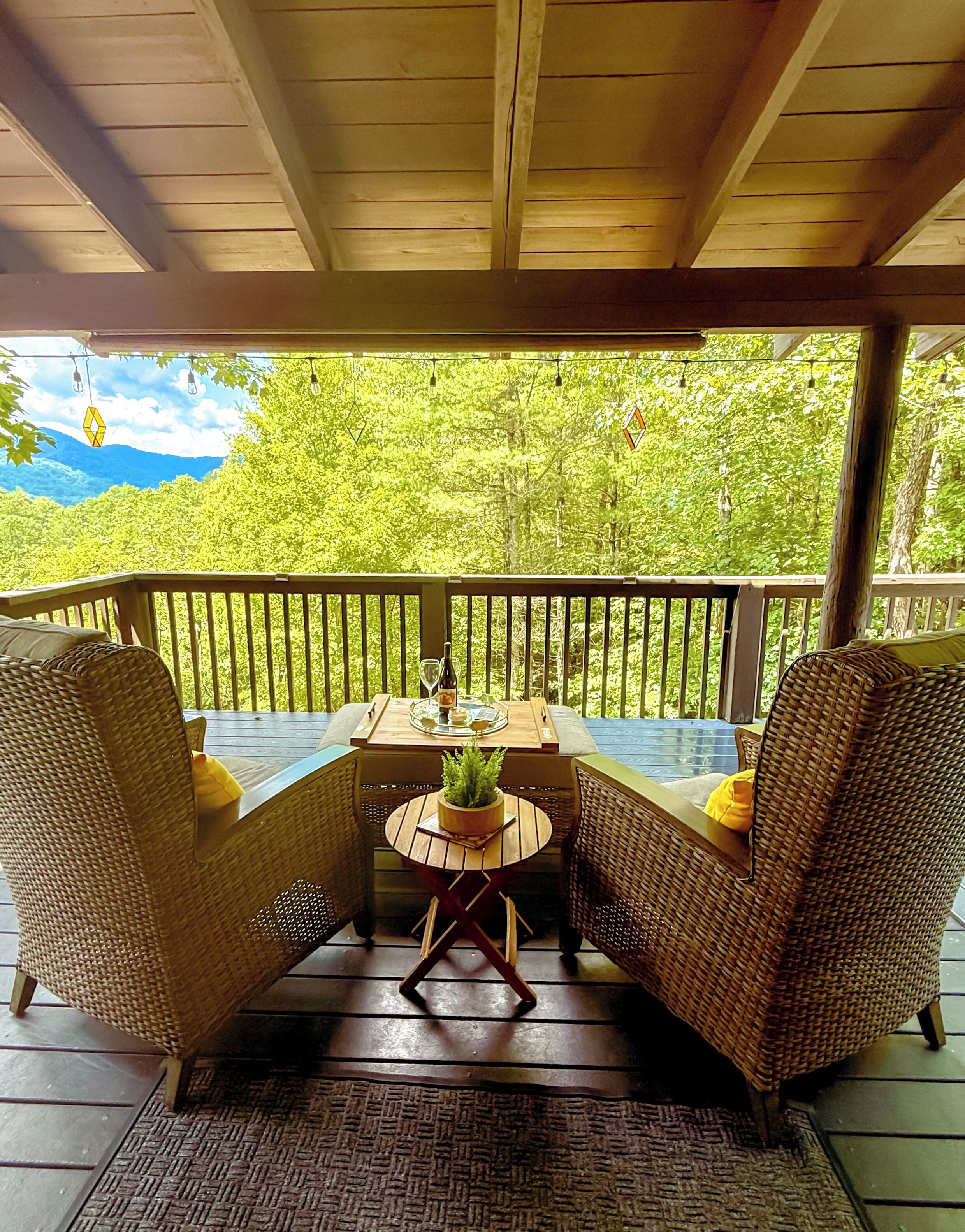 A covered outdoor seating area with wicker furniture and a table set for two, overlooking a lush green landscape.