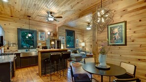 L’intérieur chaleureux d’un chalet avec des murs en bois, un coin cuisine, une table à manger avec des chaises et un ventilateur de plafond.