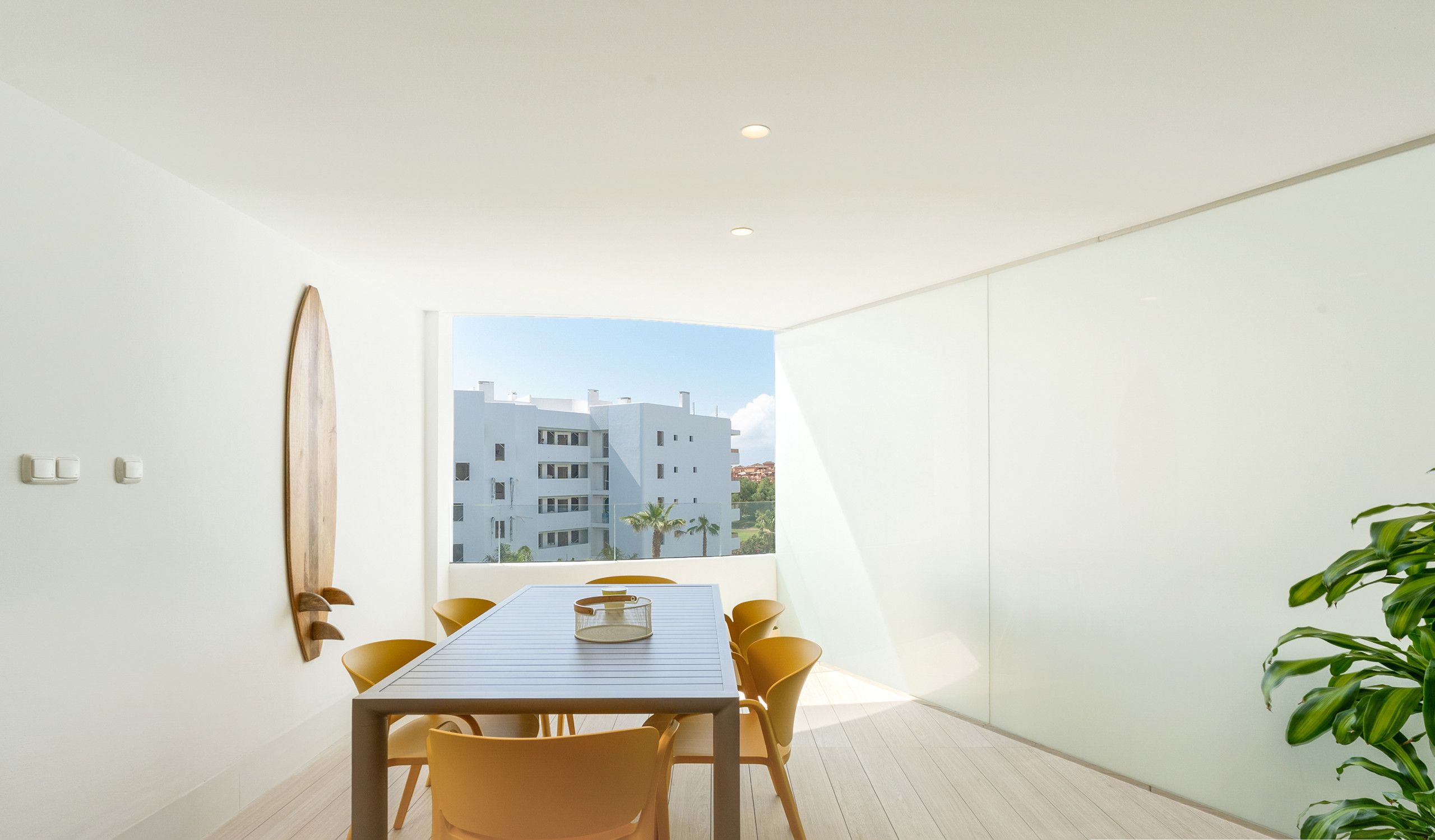 Un comedor moderno con una mesa, sillas, vistas a edificios y una planta.
