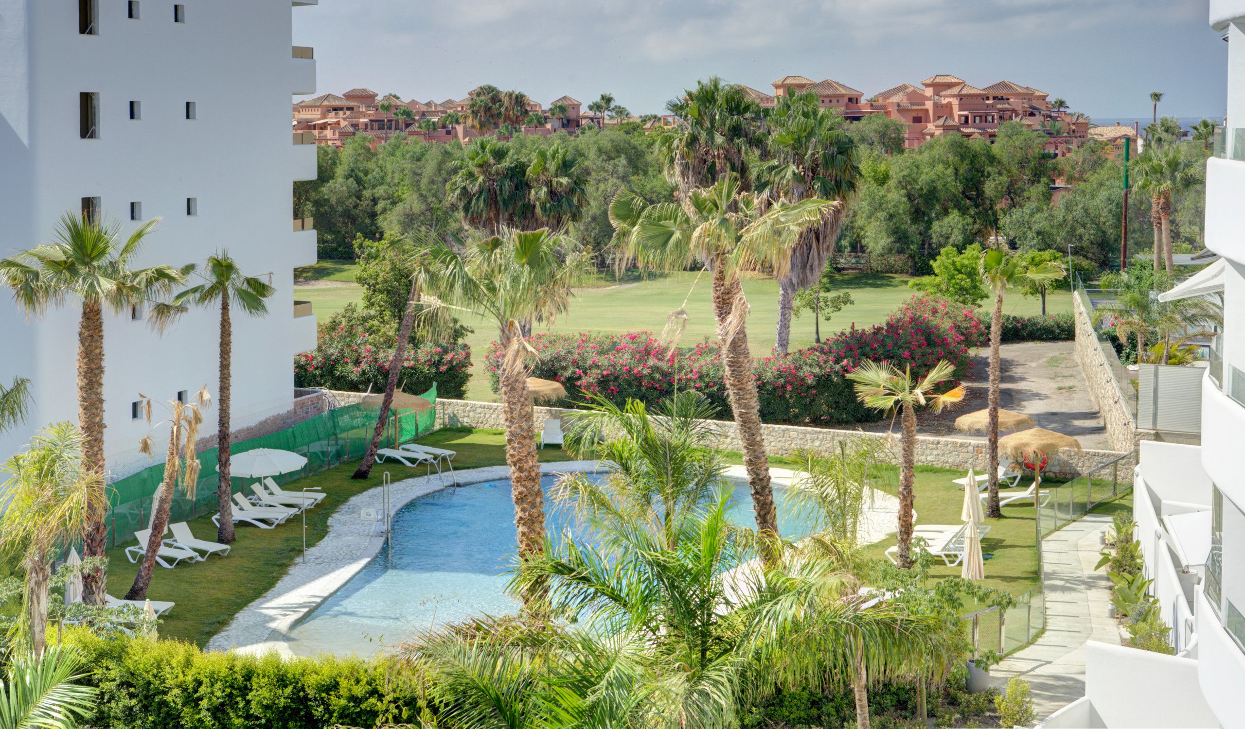 A pool surrounded by palm trees and lounge chairs, with a view of a golf course and resort buildings in the background.
