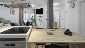 Eine moderne Küche mit Induktionskochfeld, einem Esstisch mit Stühlen, einem an der Wand befestigten Fernseher und einer Uhr.
