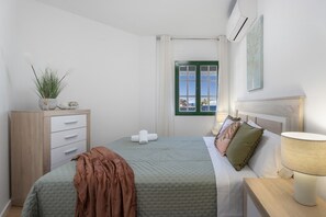 Une chambre à coucher comprenant un lit, une table de chevet, une commode, une fenêtre avec des rideaux et un climatiseur fixé au mur.