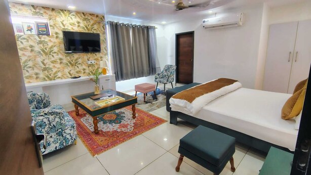 A well-lit room with a bed, a sofa, a coffee table, and a TV. - Baba Sundaram Hotel & Restaurant (Shri Madhopur)
