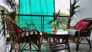 A balcony with wicker furniture, a table, and green furry ottomans. - Baba Sundaram Hotel & Restaurant (Shri Madhopur)