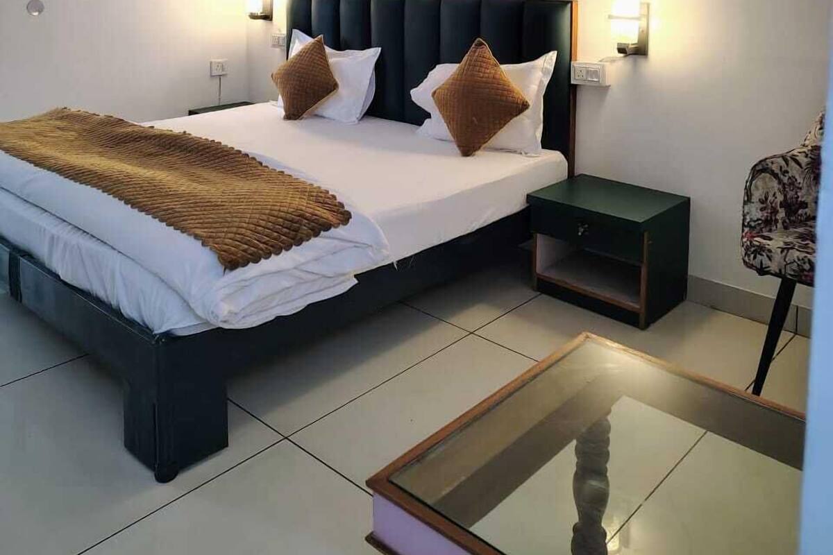 A modern hotel room with a large bed, bedside tables, a glass coffee table, and a framed picture on the wall.