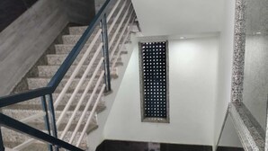A modern staircase with a metal railing, a small window with a grid pattern, and a textured wall. - Baba Sundaram Hotel & Restaurant (Shri Madhopur)