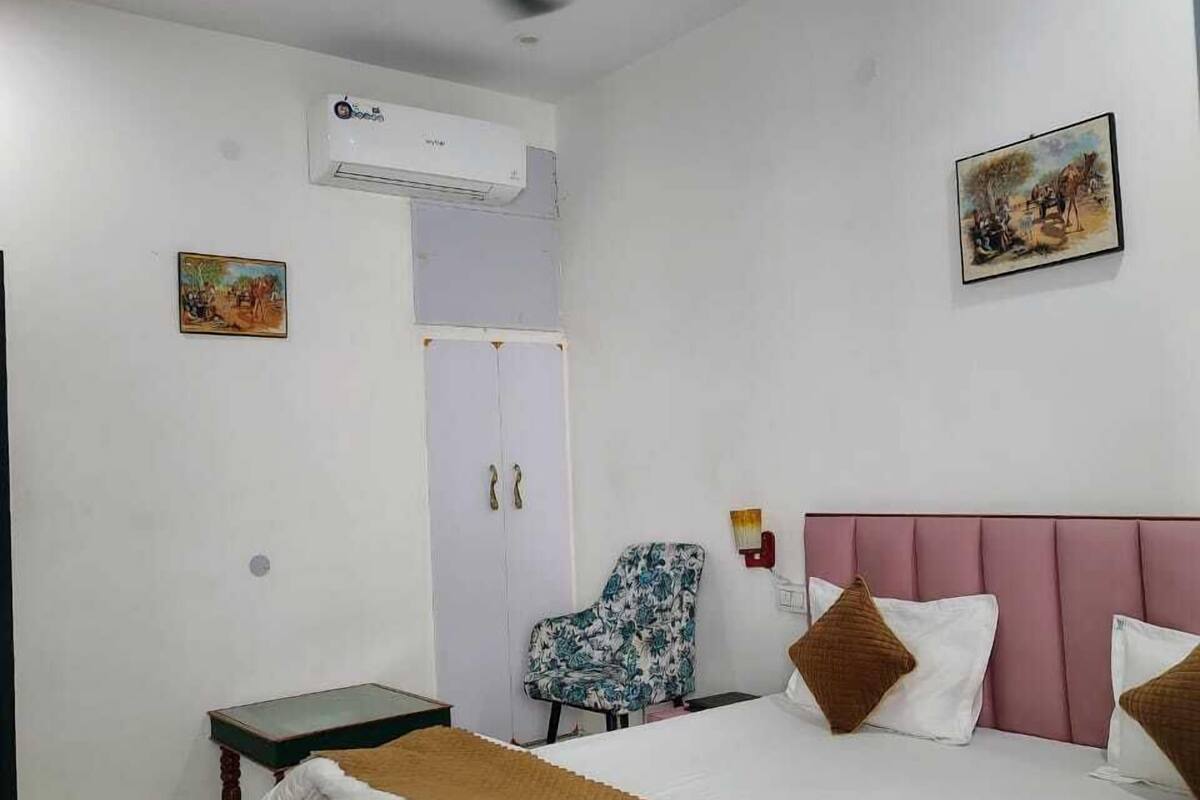 A bedroom with a bed, a ceiling fan, an air conditioner, a chair, and two paintings on the wall.