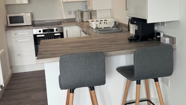 A modern kitchen with white cabinets, a microwave, a coffee maker, and two bar stools.