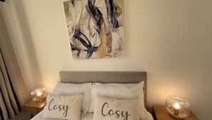 A bedroom with a bed, two bedside tables with lamps, and a wall-mounted abstract painting.
