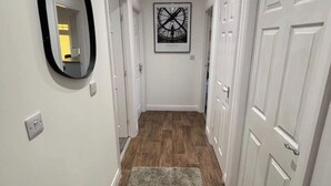 A hallway with wooden flooring, white doors, and a framed artwork on the wall.