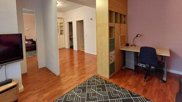 A modern living room with a wooden floor, a TV, a desk with a chair, and a patterned rug. - Quiet vacation apartment near Cologne: Hürth, centrally located (Hürth)