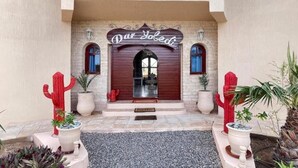 A building entrance with a sign reading "Dar Joledi," featuring a red door, two potted cacti, and a stone pathway. - Villa Dar Yobedi in Essaouira, swimming pool, hammam, ideal for families & groups (Essaouira)