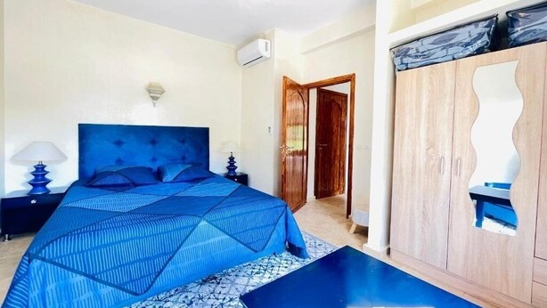 A bedroom with a large bed, a wooden wardrobe, a nightstand, and a bedside table. - Villa Dar Yobedi in Essaouira, swimming pool, hammam, ideal for families & groups (Essaouira)