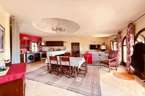 A spacious living area with a dining table, chairs, a fireplace, and a kitchen in the background.