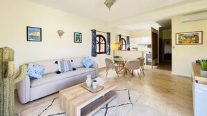 A living room with a sofa, coffee table, and a dining area with chairs and a table. - Villa Dar Yobedi in Essaouira, swimming pool, hammam, ideal for families & groups (Essaouira)