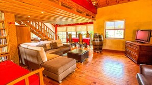 Una sala de estar acogedora con techo de madera, una escalera, chimenea y televisor.