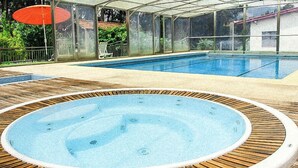 Una piscina interior con una bañera de hidromasaje, rodeada por una terraza de madera y paredes de vidrio.