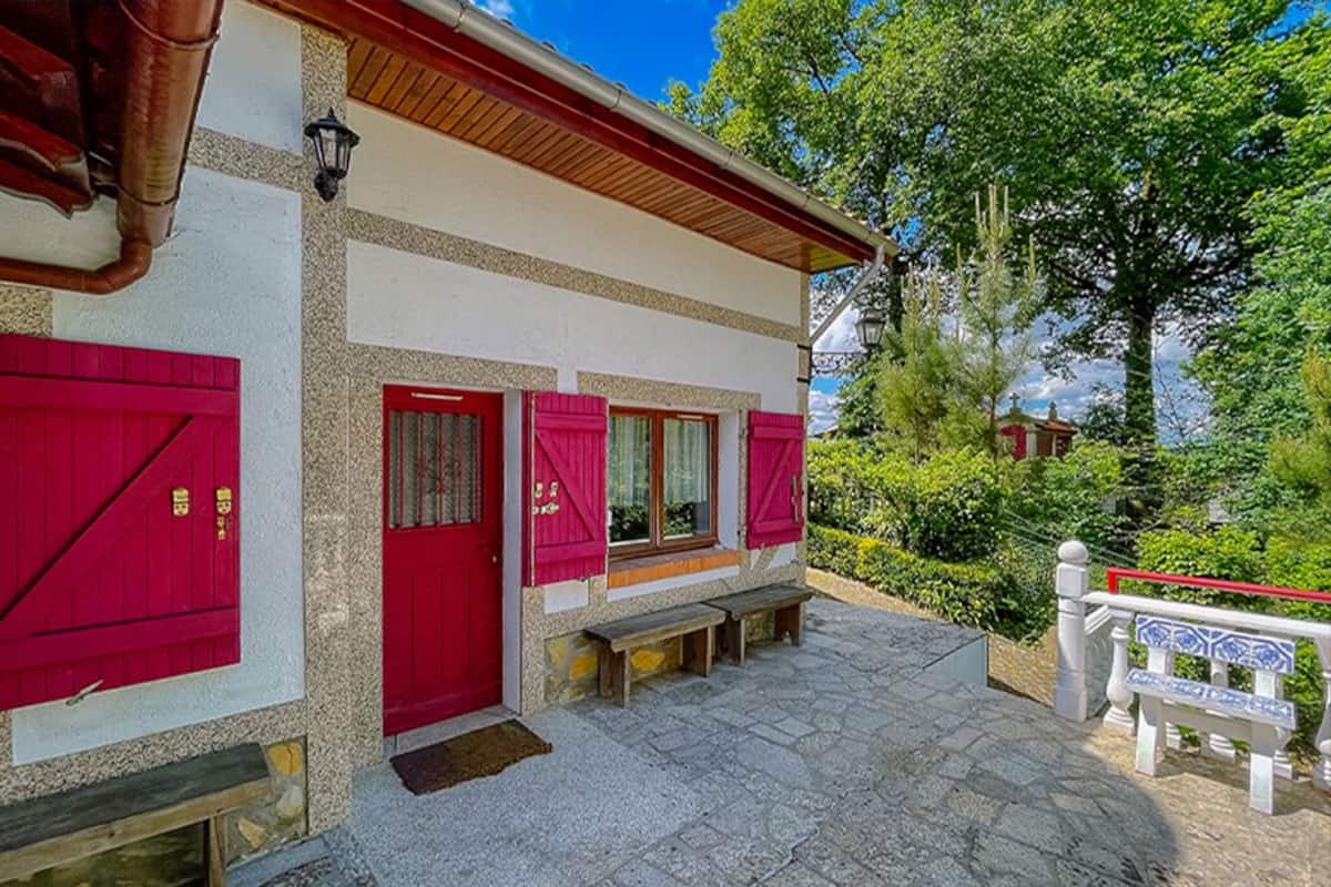 A traditional building with a red door and windows, stone steps, and a bench.