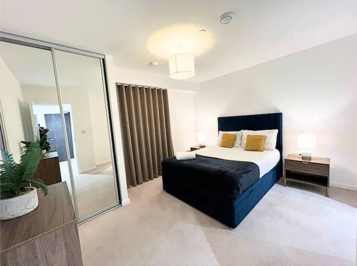 A modern hotel room with a large bed, a bedside table, a nightstand, a mirror, and a sliding door.