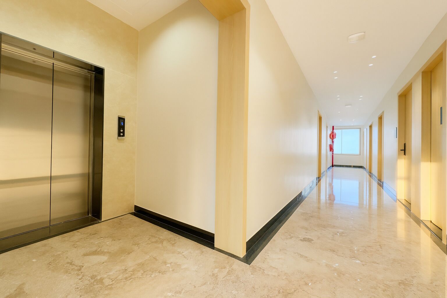A modern hallway with a marble floor, a glass elevator, and a fire extinguisher.